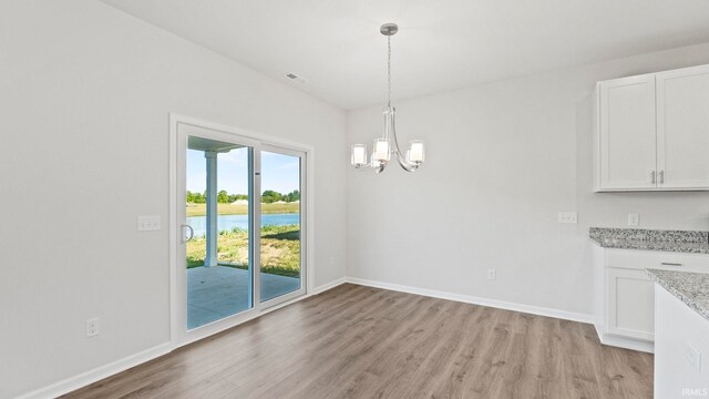 unfurnished dining area featuring a notable chandelier, light hardwood / wood-style flooring, and a water view