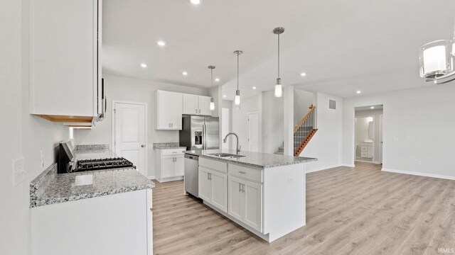 kitchen featuring stainless steel appliances, white cabinetry, an island with sink, light wood-type flooring, and light stone countertops