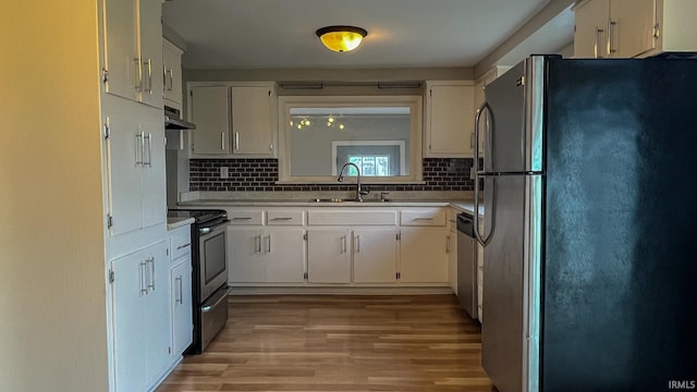 kitchen with appliances with stainless steel finishes, sink, backsplash, light hardwood / wood-style floors, and white cabinets