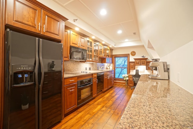 kitchen with black appliances, decorative backsplash, brown cabinetry, and hardwood / wood-style flooring