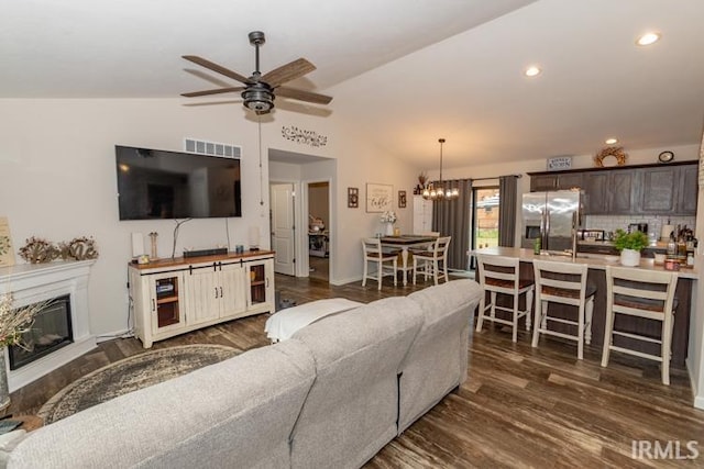 living room featuring ceiling fan with notable chandelier, dark hardwood / wood-style floors, and vaulted ceiling