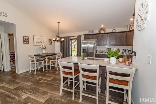 kitchen with dark wood-type flooring, stainless steel refrigerator with ice dispenser, tasteful backsplash, a notable chandelier, and lofted ceiling