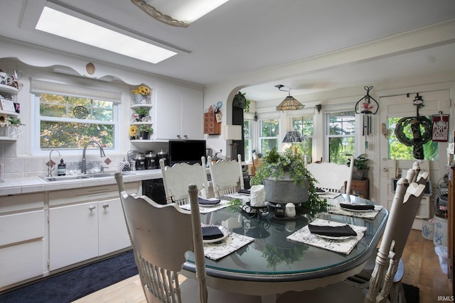 dining room with a skylight, sink, and light hardwood / wood-style flooring