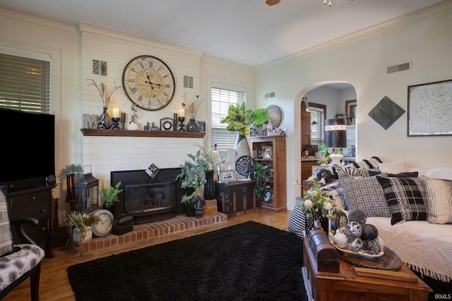 living room featuring hardwood / wood-style flooring, a brick fireplace, crown molding, and brick wall