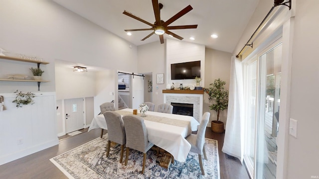 dining room featuring dark hardwood / wood-style flooring, ceiling fan, high vaulted ceiling, and a stone fireplace