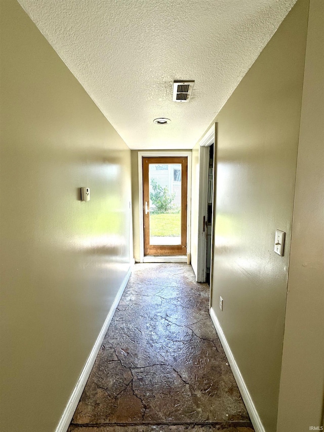 hallway with visible vents, baseboards, a textured ceiling, and stone tile floors