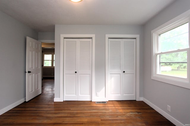 unfurnished bedroom with dark hardwood / wood-style floors and multiple closets