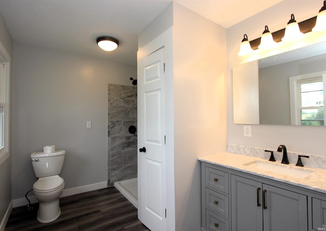 bathroom featuring vanity, a tile shower, hardwood / wood-style floors, and toilet