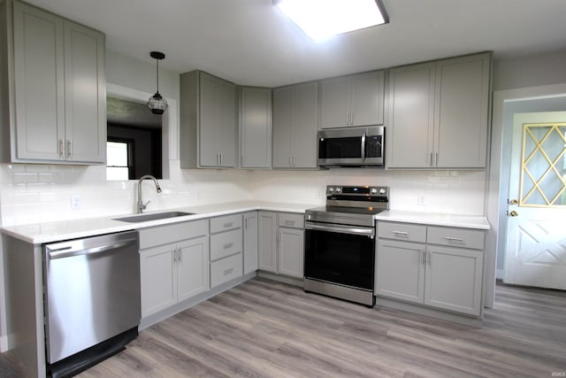 kitchen with backsplash, stainless steel appliances, sink, light wood-type flooring, and gray cabinets