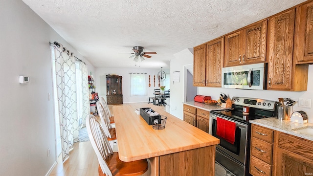 kitchen featuring a breakfast bar, appliances with stainless steel finishes, light hardwood / wood-style flooring, a textured ceiling, and ceiling fan