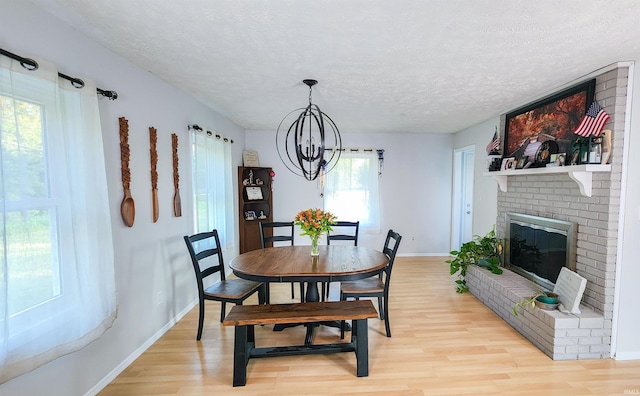 dining space featuring a chandelier, brick wall, light wood-type flooring, a fireplace, and a textured ceiling