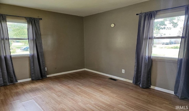 spare room featuring a healthy amount of sunlight, visible vents, baseboards, and wood finished floors