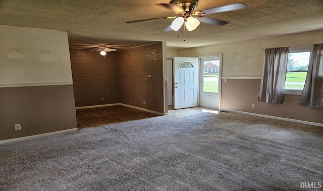 unfurnished room featuring a textured ceiling, dark colored carpet, and plenty of natural light