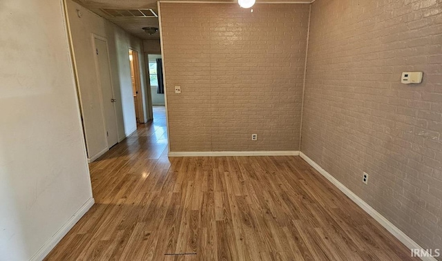 spare room with brick wall, wood finished floors, visible vents, and baseboards