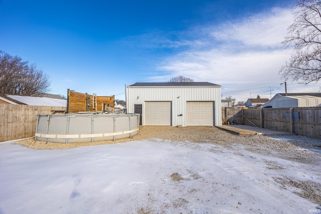 snow covered garage featuring a detached garage, fence, and a fenced in pool