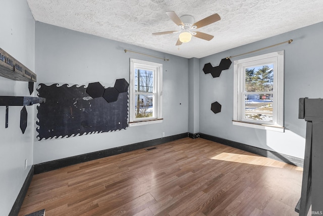 empty room with visible vents, a textured ceiling, baseboards, and wood finished floors