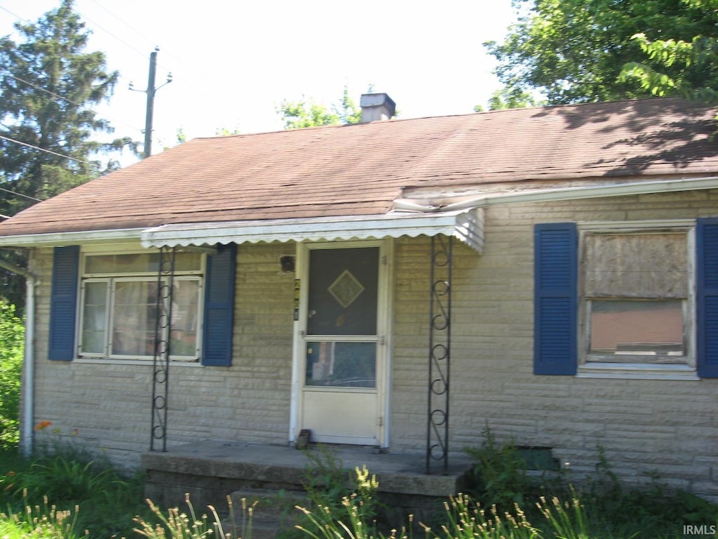 view of front facade featuring a shingled roof and a chimney