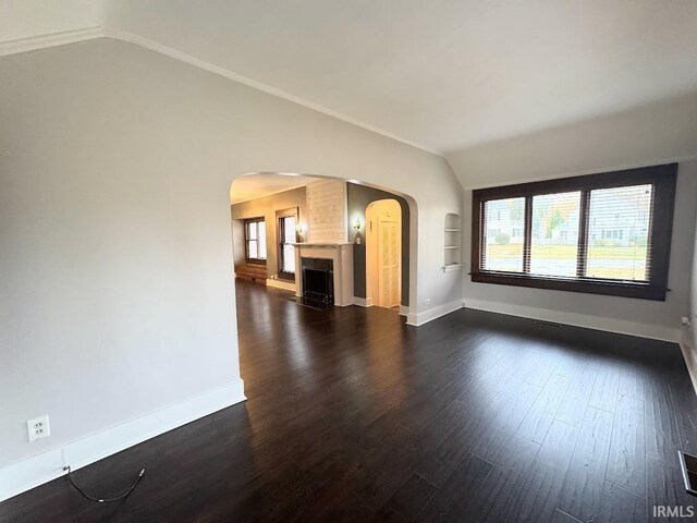 unfurnished living room featuring vaulted ceiling, baseboards, arched walkways, and dark wood-type flooring