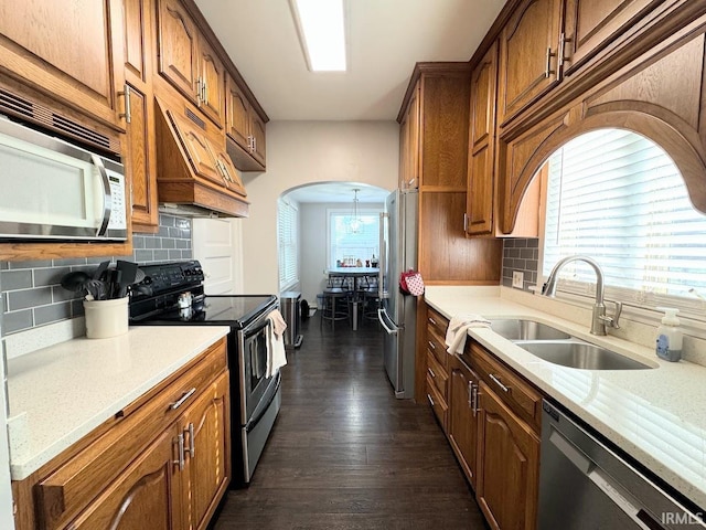 kitchen with arched walkways, a sink, dark wood-type flooring, appliances with stainless steel finishes, and brown cabinets