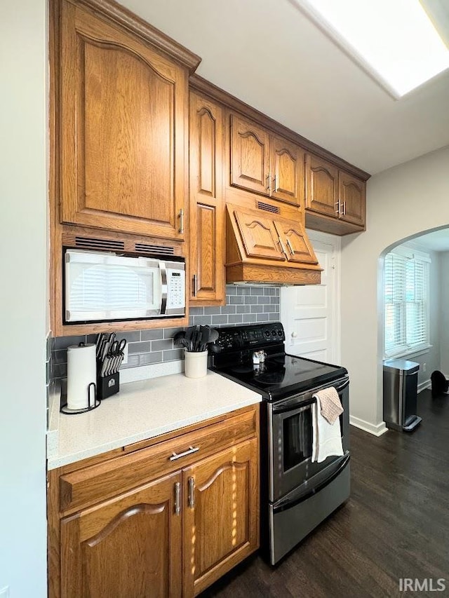 kitchen featuring brown cabinetry, stainless steel electric range, premium range hood, and white microwave