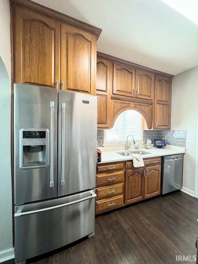 kitchen featuring a sink, backsplash, stainless steel appliances, light countertops, and dark wood-style flooring