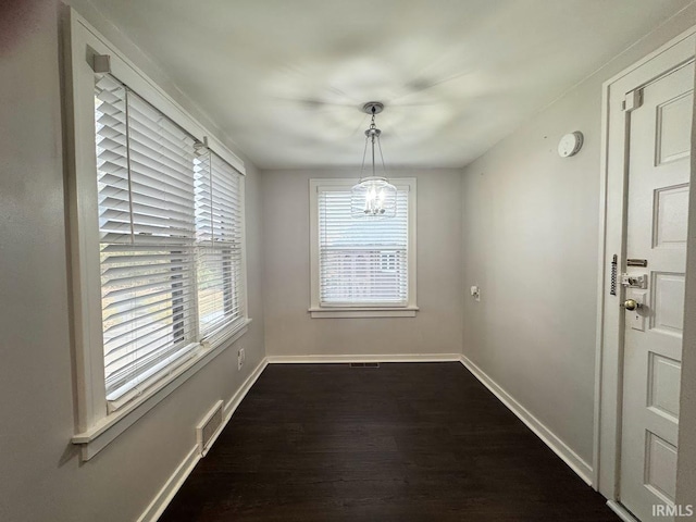 unfurnished dining area featuring dark wood-style floors, visible vents, an inviting chandelier, and baseboards