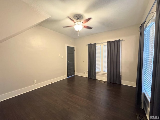 unfurnished room with ceiling fan, visible vents, baseboards, and dark wood-style floors