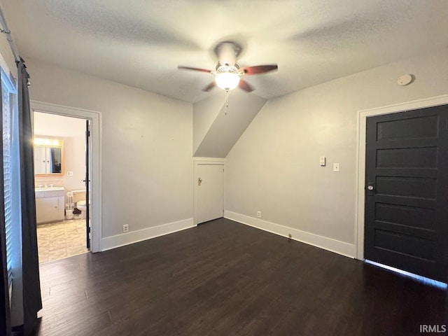 additional living space with baseboards, a textured ceiling, dark wood-style floors, and a ceiling fan