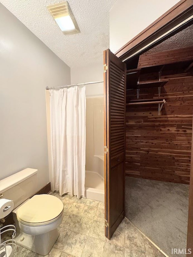 bathroom featuring wooden walls, toilet, lofted ceiling, a shower with curtain, and a textured ceiling