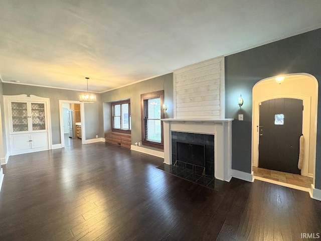 unfurnished living room with baseboards, dark wood finished floors, ornamental molding, a fireplace, and an inviting chandelier