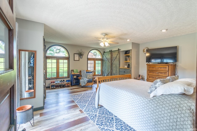 bedroom featuring a textured ceiling, ceiling fan, light wood-type flooring, and a barn door