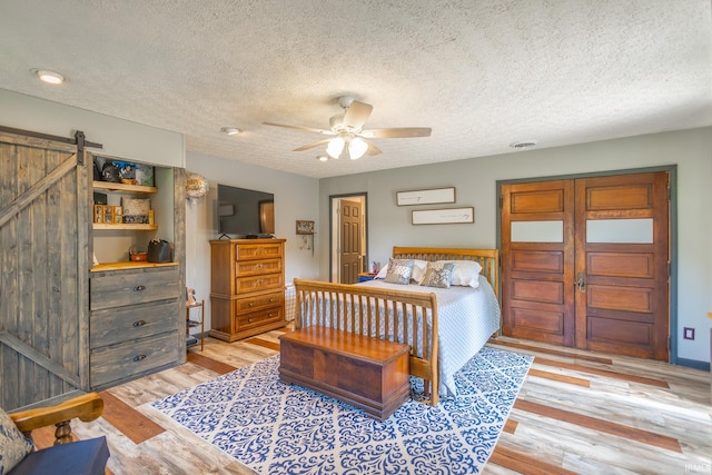 bedroom featuring ceiling fan, a textured ceiling, light hardwood / wood-style floors, and a barn door