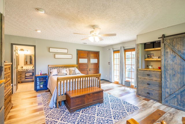 bedroom with ceiling fan, a barn door, light hardwood / wood-style flooring, and a textured ceiling