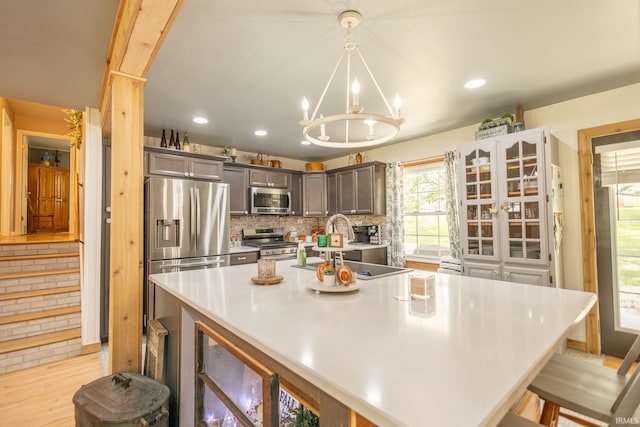 kitchen with light hardwood / wood-style flooring, pendant lighting, a chandelier, tasteful backsplash, and appliances with stainless steel finishes