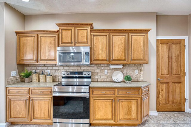 kitchen with light tile patterned floors, stainless steel appliances, decorative backsplash, and a textured ceiling