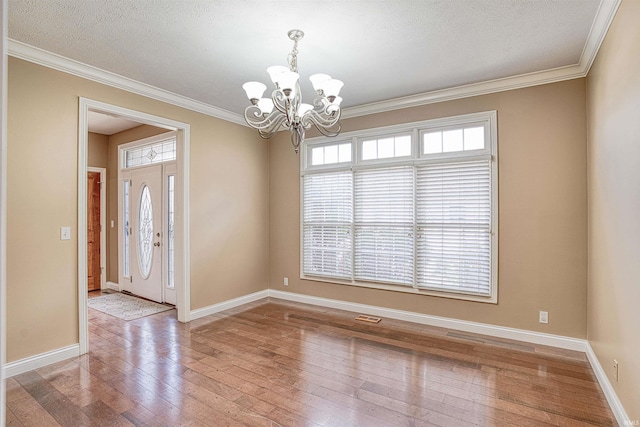 empty room featuring a textured ceiling, ornamental molding, hardwood / wood-style floors, and an inviting chandelier