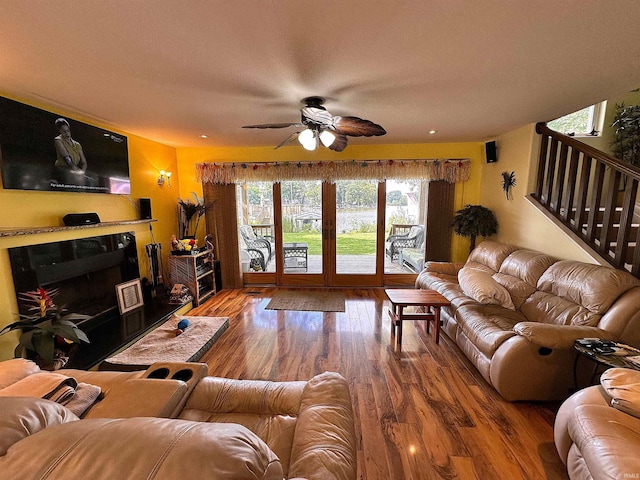 living room with a wealth of natural light, wood finished floors, a ceiling fan, and stairs