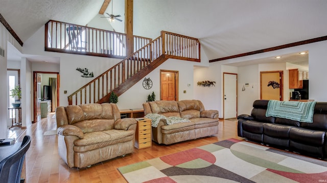 living room featuring ceiling fan, high vaulted ceiling, light wood-style flooring, visible vents, and stairway