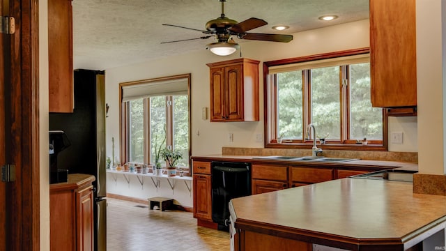 kitchen featuring black dishwasher, freestanding refrigerator, a healthy amount of sunlight, a sink, and a peninsula