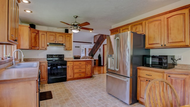 kitchen featuring light countertops, a sink, ceiling fan, under cabinet range hood, and black appliances