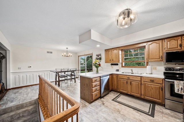 kitchen featuring sink, hanging light fixtures, appliances with stainless steel finishes, a chandelier, and kitchen peninsula