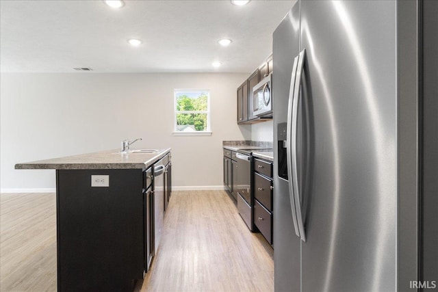 kitchen with baseboards, an island with sink, light wood-style flooring, appliances with stainless steel finishes, and a sink