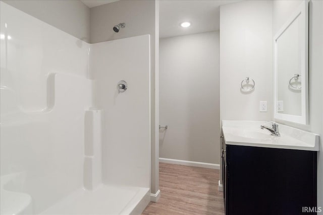 full bathroom featuring wood finished floors, walk in shower, vanity, and baseboards