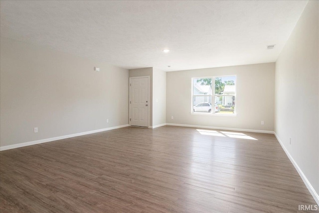 empty room featuring wood finished floors, visible vents, and baseboards