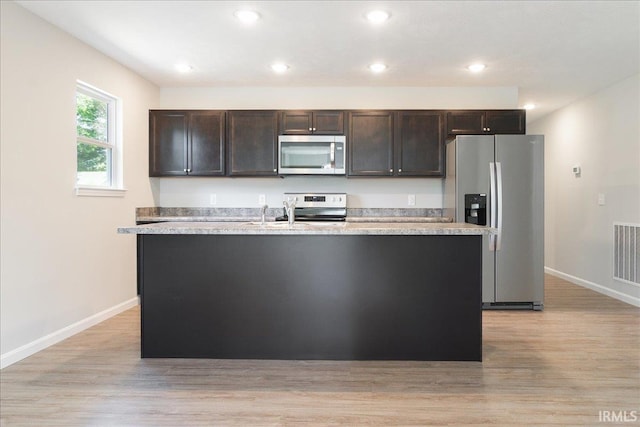 kitchen featuring light wood-type flooring, a center island with sink, stainless steel appliances, and light countertops