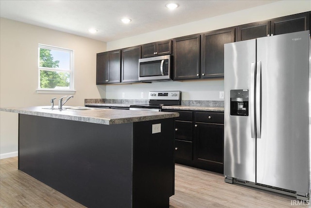 kitchen with light wood-style floors, a center island with sink, stainless steel appliances, and a sink