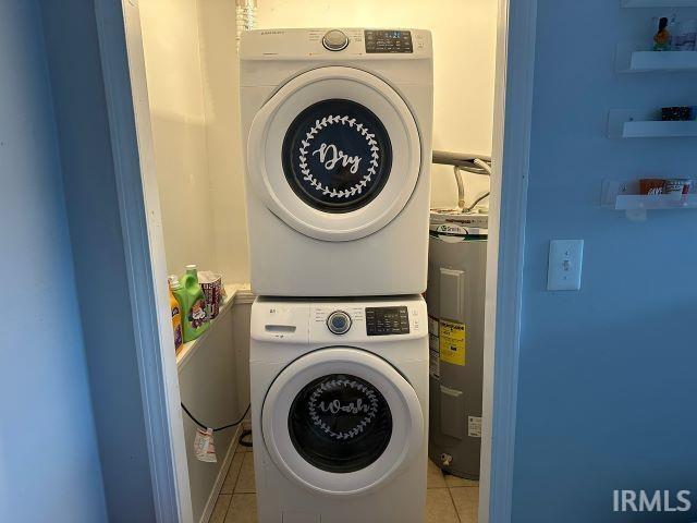 washroom featuring stacked washer and dryer, water heater, and light tile patterned floors