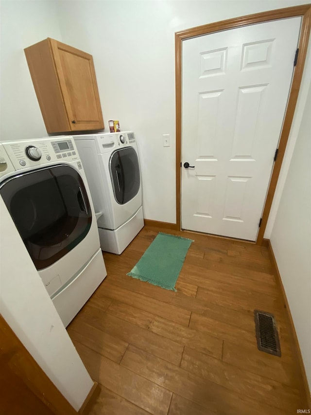 laundry area featuring cabinets, hardwood / wood-style floors, and separate washer and dryer