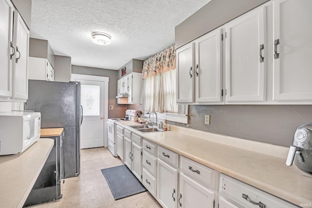 kitchen featuring white cabinetry, sink, a textured ceiling, white appliances, and light tile patterned flooring