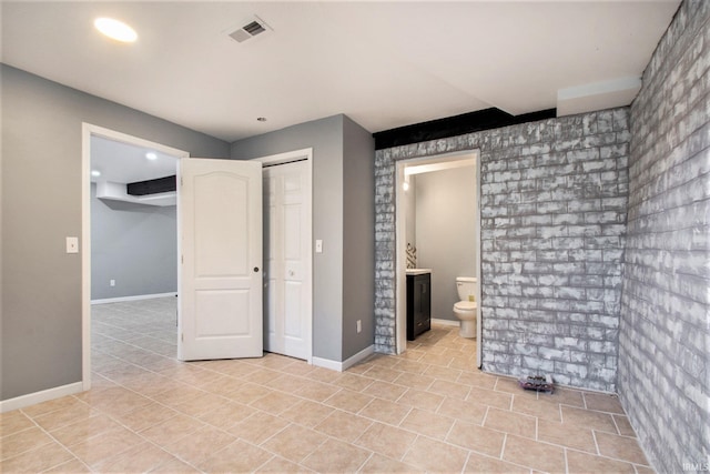 unfurnished bedroom featuring a closet, brick wall, light tile patterned floors, and ensuite bath